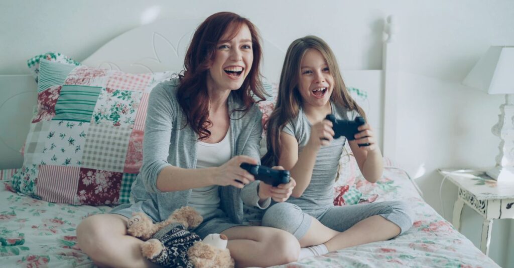 スマホやタブレットを囲んで、家族全員で一緒に笑いながらゲームを楽しんでいる様子の画像。世代を超えて盛り上がる雰囲気。