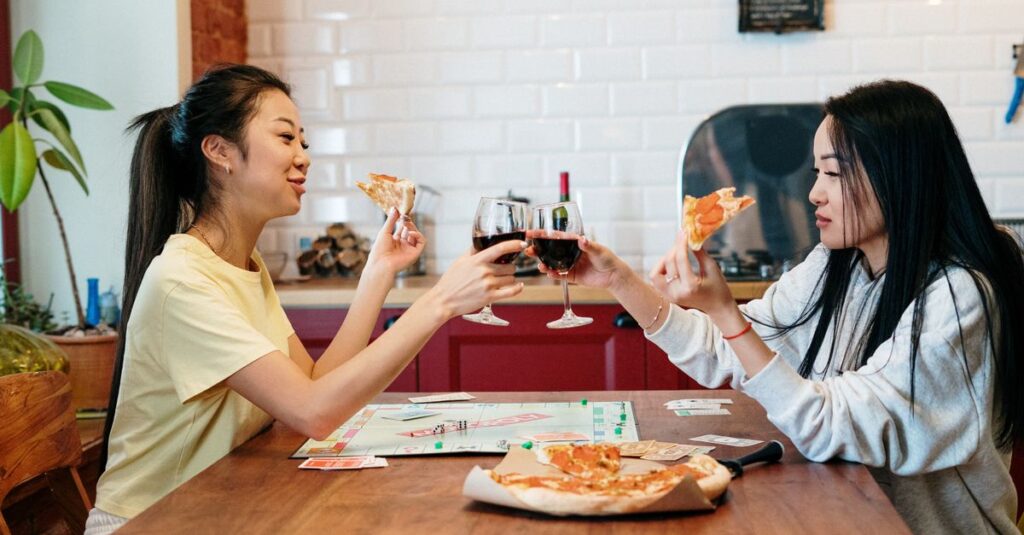 冷たい飲み物とお菓子が並ぶ中、ボードゲームを囲んで笑顔の人々が夏の室内で楽しんでいる様子