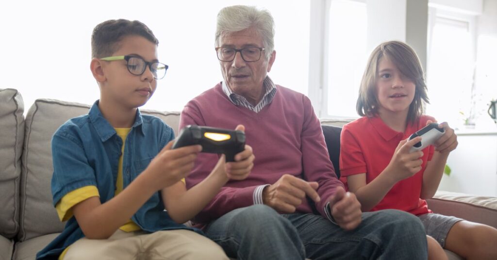 幼児から祖父母まで世代を超えて室内ゲームを楽しむ家族。笑顔で遊ぶ様子が伝わる16:9写真。